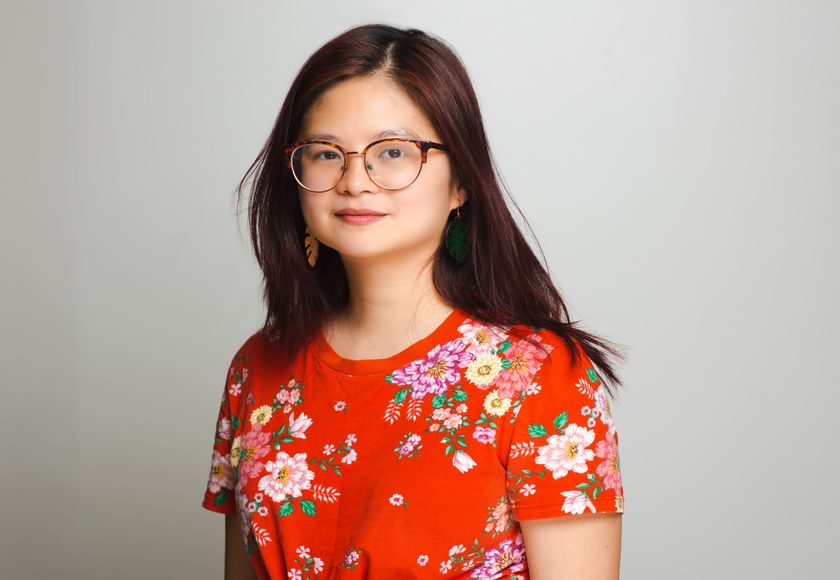 A woman with glasses. She has long dark hair and is dressed in a red floral top.